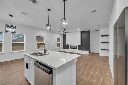 Kitchen featuring white cabinetry, sink, hanging light fixtures, stainless steel appliances, and a center island with sink