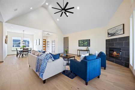 Living room with light hardwood / wood-style flooring, high vaulted ceiling, a tile fireplace, and ceiling fan with notable chandelier