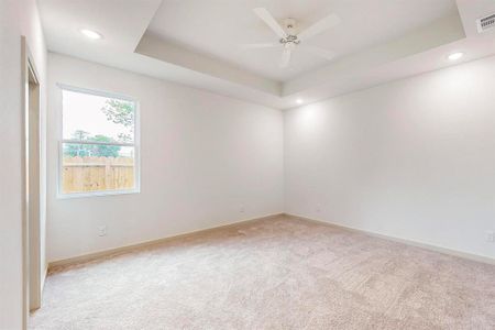 Spare room with a tray ceiling, light colored carpet, and ceiling fan