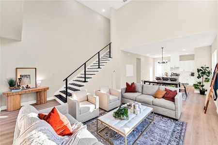 Living room with light wood-type flooring, a high ceiling, and an inviting chandelier