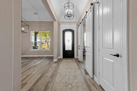 Foyer with a barn door, a notable chandelier, crown molding, lofted ceiling, and hardwood / wood-style flooring