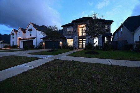 This photo showcases a modern two-story home with a stone facade and large windows, set in a suburban neighborhood. The house features a well-maintained front yard and a spacious driveway.