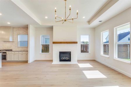 Unfurnished living room with a raised ceiling, light hardwood / wood-style flooring, a notable chandelier, and a brick fireplace