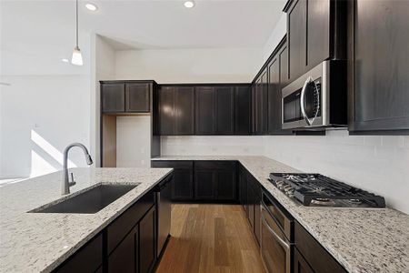 Kitchen with light stone countertops, stainless steel appliances, sink, dark hardwood / wood-style floors, and hanging light fixtures