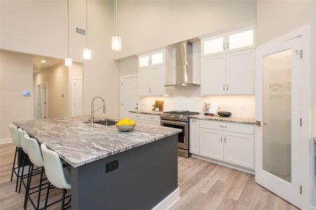 Kitchen with lots of cabinets, hanging light fixtures, wall chimney range hood, a towering ceiling, and gas stove