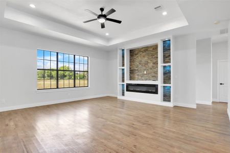 Unfurnished living room featuring ceiling fan, light hardwood / wood-style floors, and a tray ceiling