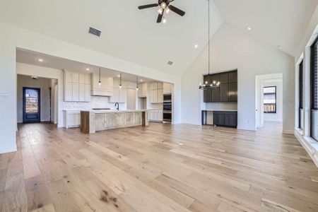 Unfurnished living room with ceiling fan with notable chandelier, light hardwood / wood-style floors, and high vaulted ceiling