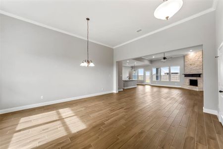 Unfurnished living room featuring a fireplace, ceiling fan with notable chandelier, and crown molding