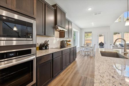 Kitchen with stainless steel microwave, sink, black electric cooktop, decorative light fixtures, and light hardwood / wood-style floors