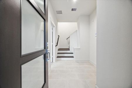 The inviting entryway of this modern home sets the tone for the stylish interiors. Clean tile flooring and an open layout create a bright and welcoming space. Just inside the entrance, you are greeted by a sleek staircase that leads to the main living areas and a first-floor bedroom, offering a harmonious flow between the floors. The design is minimal yet functional, providing a smooth transition from the outdoors into the home.