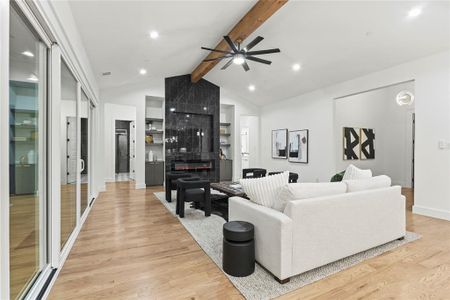 Living area featuring baseboards, a ceiling fan, light wood-style flooring, beamed ceiling, and a fireplace