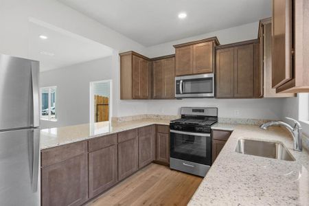 Kitchen with light stone counters, recessed lighting, appliances with stainless steel finishes, a sink, and light wood-type flooring