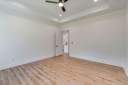 Empty room with ceiling fan, light wood-type flooring, and a tray ceiling