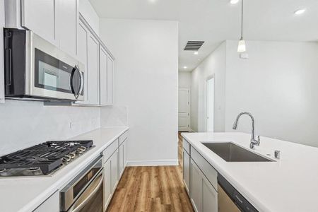 Kitchen with decorative backsplash, pendant lighting, stainless steel appliances, light hardwood / wood-style flooring, and sink