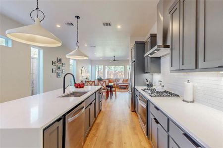 Kitchen with stainless steel appliances, wall chimney range hood, sink, a kitchen island with sink, and light wood-type flooring