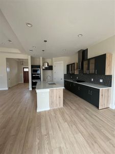 Kitchen with hanging light fixtures, sink, light hardwood / wood-style flooring, an island with sink, and extractor fan