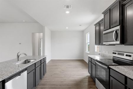 Kitchen featuring sink, stainless steel appliances, light wood-style floors, and light stone counters