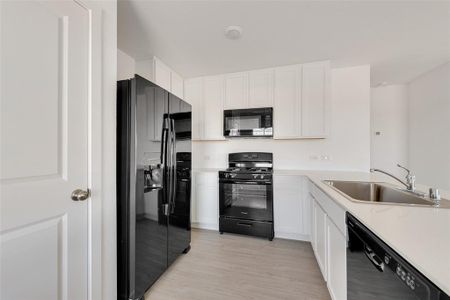 Kitchen with white cabinetry, sink, black appliances, and light hardwood / wood-style flooring