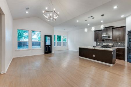 Kitchen with light wood-type flooring, a chandelier, dark brown cabinets, stainless steel appliances, and an island with sink