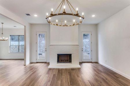 Unfurnished living room featuring a brick fireplace, wood-type flooring, and a chandelier