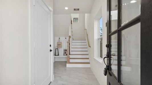 Enter thru the front door to be greeted by bright, clean entryway with a staircase leading up. The space features modern finishes with a tiled floor, natural light from a window, and a welcoming, neutral color palette.