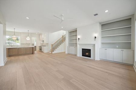 This open-concept living area seamlessly connects comfort and functionality. The living room, anchored by a gas fireplace and custom built-ins, flows effortlessly into the gourmet kitchen, creating an inviting space for both relaxation and entertaining. The kitchen features a spacious island with natural wood cabinetry, pendant lighting, and quartz countertops, complemented by a designer backsplash and high-end stainless appliances.