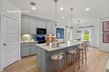 Kitchen featuring gray cabinetry, black appliances, light hardwood / wood-style floors, decorative light fixtures, and a center island with sink