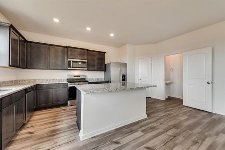 Kitchen featuring light hardwood / wood-style floors, appliances with stainless steel finishes, light stone countertops, and a kitchen island