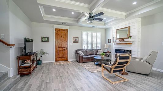 Living room featuring beamed ceiling, a fireplace, light hardwood / wood-style flooring, ornamental molding, and ceiling fan