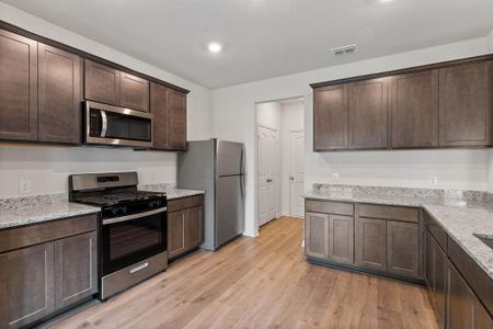 Kitchen with light wood-style flooring, dark cabinetry, stainless steel appliances, and light stone counters