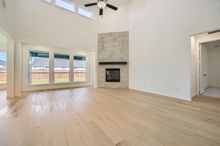 Unfurnished living room with a high ceiling, light hardwood / wood-style flooring, a tiled fireplace, and ceiling fan