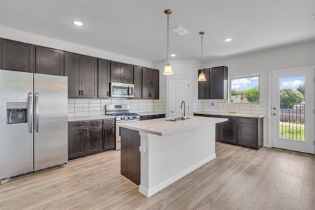 Kitchen featuring stainless steel appliances, light hardwood / wood-style floors, backsplash, and an island with sink