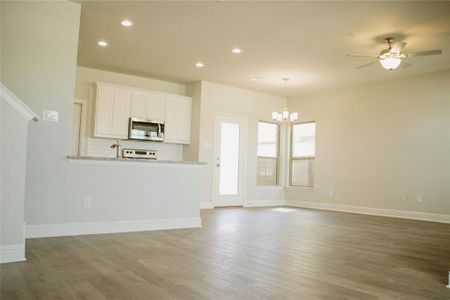 Unfurnished living room featuring ceiling fan with notable chandelier and dark wood-type flooring