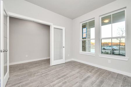 At the forefront, a refined home office beckons productivity and focus. Luxurious details like elegant wood look tile, custom paint, expansive windows with privacy blinds, and French doors create an inspiring workspace. Sample photo of completed home with similar floor plan. As-built interior colors and selections may vary.