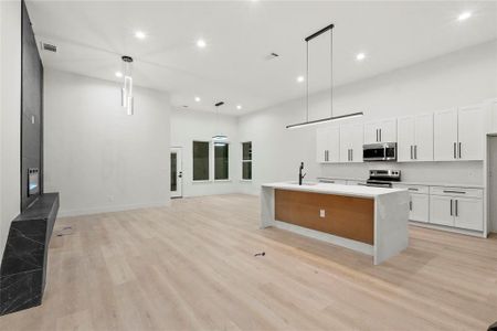 Kitchen featuring appliances with stainless steel finishes, light hardwood / wood-style flooring, an island with sink, white cabinets, and hanging light fixtures