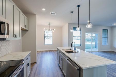 Kitchen featuring sink, stainless steel appliances, decorative light fixtures, light stone countertops, and a center island with sink