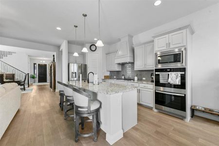 Kitchen featuring premium range hood, light stone countertops, appliances with stainless steel finishes, an island with sink, and white cabinets