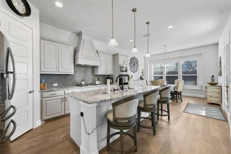 Kitchen featuring light stone countertops, custom exhaust hood, decorative light fixtures, stainless steel appliances, and a kitchen island with sink