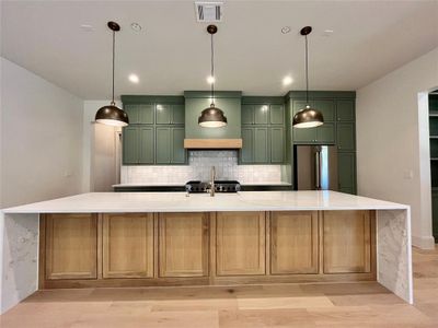 Kitchen with a large island with sink, high quality fridge, backsplash, and light hardwood / wood-style floors