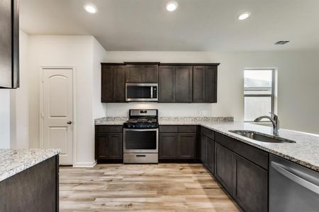 Kitchen featuring light wood-type flooring, appliances with stainless steel finishes, light stone counters, sink, and dark cabinetry