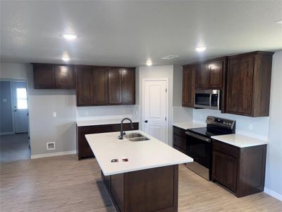 Kitchen with light hardwood / wood-style flooring, appliances with stainless steel finishes, sink, a center island with sink, and dark brown cabinetry