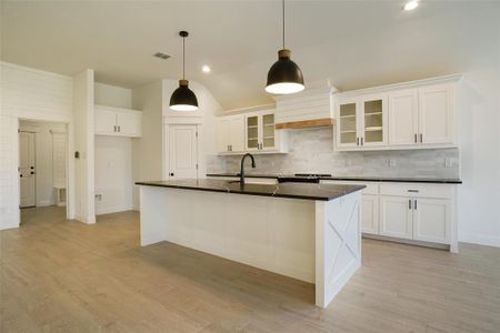 Kitchen with a kitchen island with sink, pendant lighting, tasteful backsplash, and custom range hood