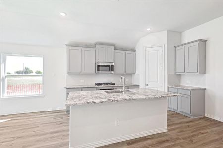 Kitchen featuring appliances with stainless steel finishes, gray cabinetry, light hardwood / wood-style floors, vaulted ceiling, and a kitchen island with sink