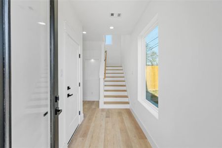 A striking entryway featuring a dark-framed door with glass panel, perfectly paired with a large window flooding the space with natural light as it highlights the vinyl wide plank wood-like floors.