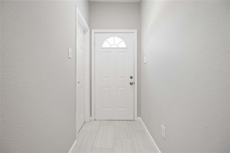 Bright and welcoming entryway with neutral walls, a white door, and light tile flooring.