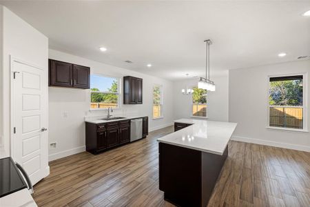 Kitchen featuring a center island, sink, hanging light fixtures, stainless steel dishwasher, and dark brown cabinets