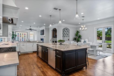 Kitchen featuring sink, wood-type flooring, ceiling fan with notable chandelier, a center island with sink, and white cabinets