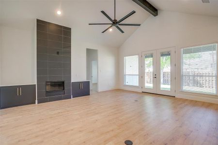 Unfurnished living room with ceiling fan, a tiled fireplace, french doors, light wood-type flooring, and high vaulted ceiling