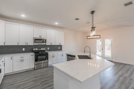 Kitchen with stainless steel appliances, a sink, visible vents, white cabinetry, and tasteful backsplash