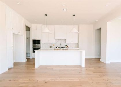 Kitchen with a kitchen island with sink, pendant lighting, light hardwood / wood-style flooring, appliances with stainless steel finishes, and white cabinets